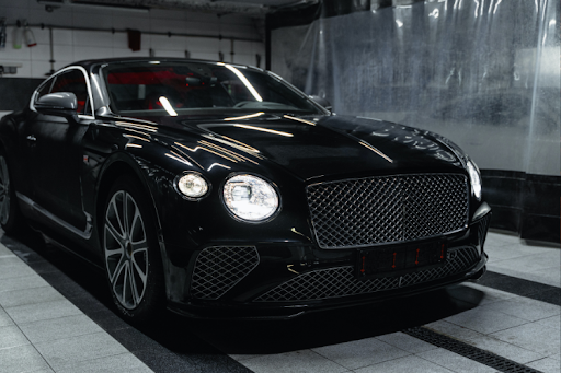 Luxury black sports car with distinctive grille and headlights parked indoors in a showroom or garage.