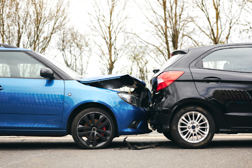 Car accident scene showing a blue vehicle crashed into the rear of a black car on the road.