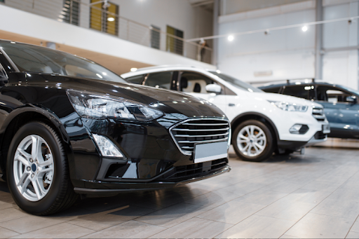 Row of new cars displayed in a modern car dealership showroom.