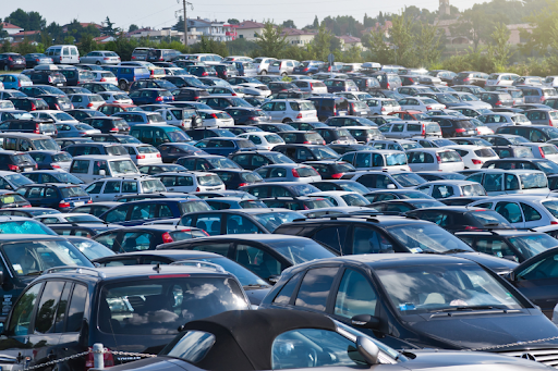 Large crowded parking lot filled with rows of parked cars of different makes and models.