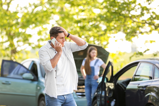 Car crash scene with a man making a call and another driver standing nearby.