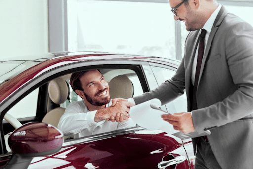 Driver in a red car smiling while greeting an insurance representative.