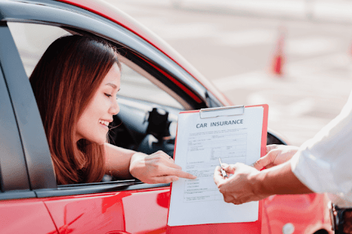 Woman in a red car reviewing a car insurance document with an agent.