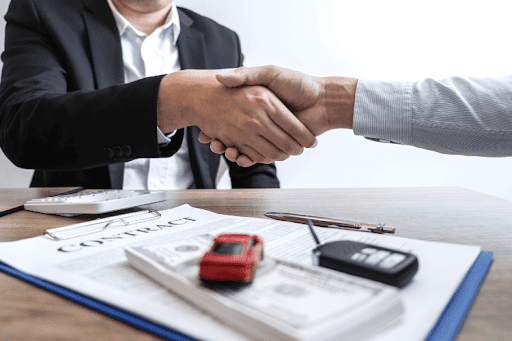 Insurance agent and client shaking hands over a contract form.