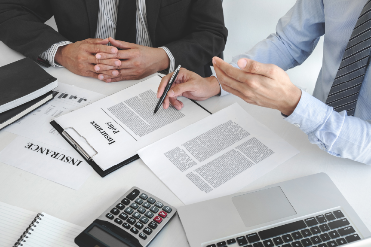 Insurance agent reviewing policy documents with a client at a desk.