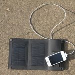 foldable solar panel for travel layed out on the grass charging a smartphone