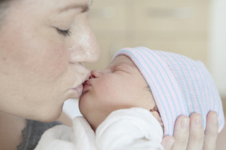 A mother gently kissing her newborn baby who is wearing a striped hat.