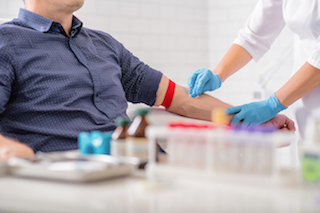 A healthcare professional drawing blood from a patient's arm, with vials and other medical supplies on a table.