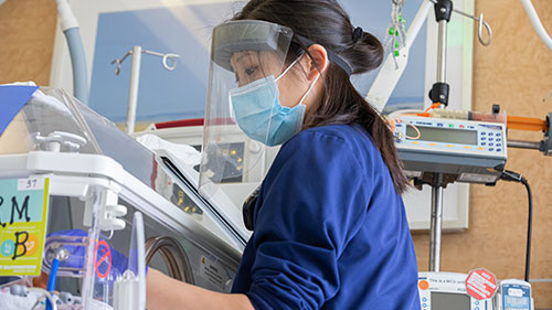 Female nurse wearing PPE and a face shield in a labor and delivery room