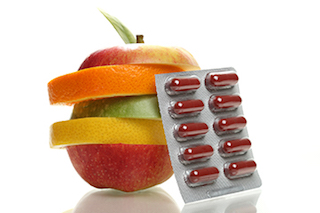 A sliced apple with layers of different fruits stacked together, next to a blister pack of red capsules.