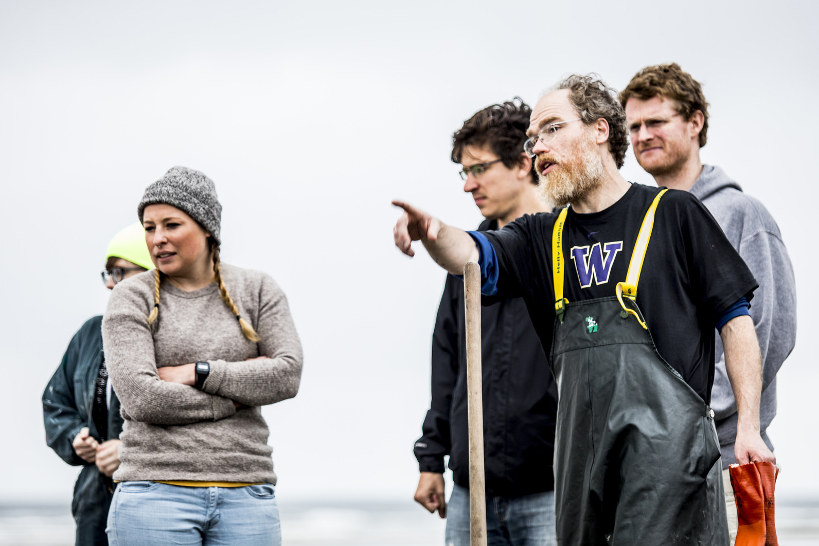 Outdoor shot of man in UW logo shirt pointing and a group of people listening to him