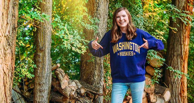 Hannah Doyle, a Unite UW participant, smiling while walking in the woods in a UW sweatshirt