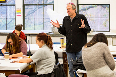man standing up and talking to students sitting at long tables