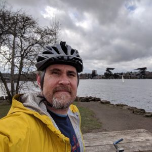 A photo of Greg Barnes on his bike with Husky Stadium in the background.