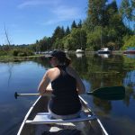 A woman sits in the front of a canoe on the water; a building marked with the UW logo is on her right.