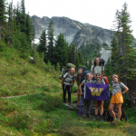 First Year Adventures hikers pose with the UW flag against a backdrop of trees, grass, and the trail.
