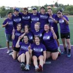 Softball team Champs Backdoor Sliders gather smiling on the field wearing purple Champs shirts.