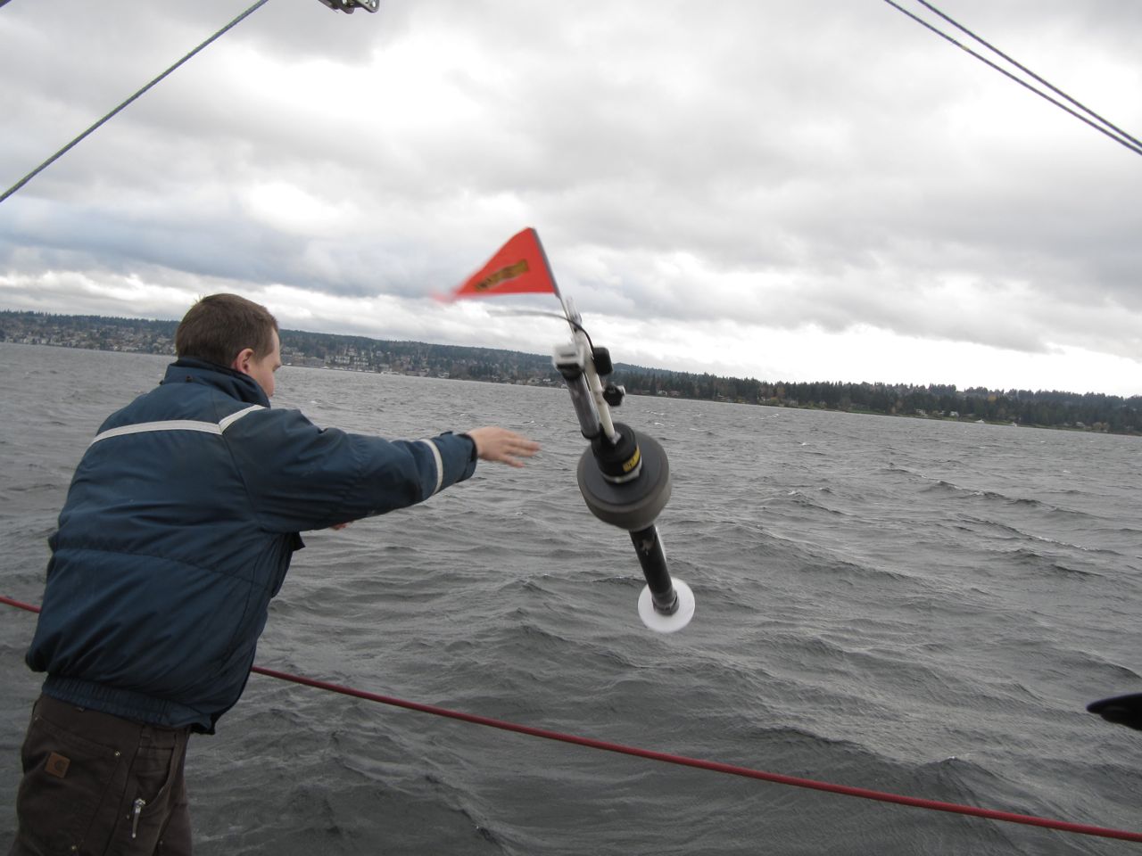 a photograph of the scientist throwing a long, tubular buoy with a red flag on top from a ship into the water.