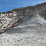 Large cliff of white ashy material surrounded by rock cliffs when two researchers working the face