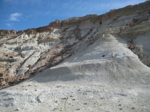 Large cliff of white ashy material surrounded by rock cliffs when two researchers working the face