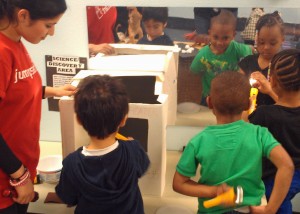 College student helps three children shine flashlights in a mirror