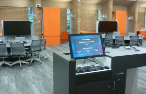 An instructor's station is ready for use in an active-learning classroom. Each table is fully wired and has space for nine students.