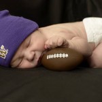 Baby asleep wearing purple cap and holding tiny football
