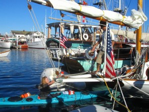 Woman in kayak hands device to man n his sailboat