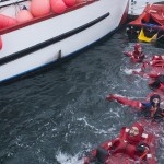 Six swimmers in survival suits float in a row in water