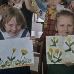Two girls hold up similar drawings of flowers