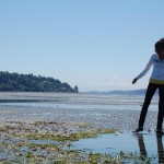 Girl on the shoreline with mountain in background.