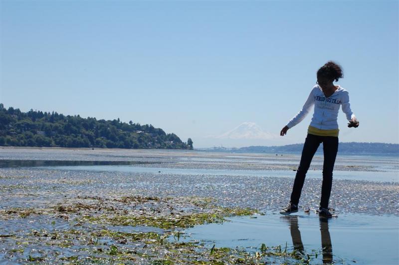 Girl on the shoreline with mountain in background.