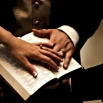 Hands of a man and woman wearing weddng rings on to pf open bible