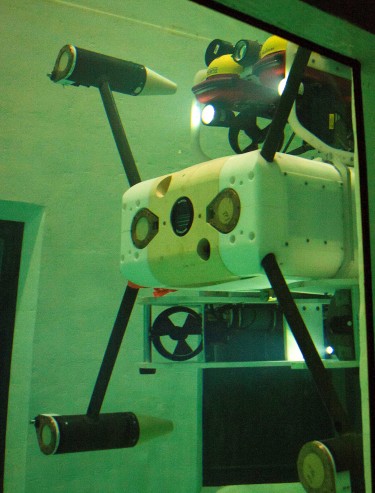The Millennium Falcon robot maneuvers underwater in a testing tank on campus. The monitoring instruments (white box in the middle) are guided by the robot's thrusters toward a docking station on the bottom of the tank. Researchers controlled the machine from above.