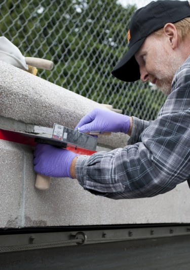 A facilities maintenance mason repairs grout along the fountain’s rim.