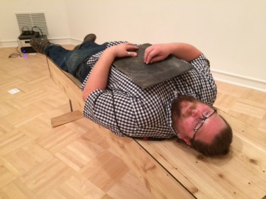 Artist Benjamin Gale-Schreck lies on his "coffin-cradle." He invites people to lie down on it and experience the sounds and vibrations he creates. A lot of his work relates to experiences with family, he said, back in El Paso, Illinois, where his late father started an arts center. This is at the annual MFA/M-DEsign show at the University of Washington's Henry Art Gallery.