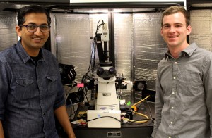 Two people standing next to a microscope.