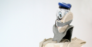 Image: Lizzi Bougatsos. Self–portrait, 2009. Donald Duck mask, fluorescent Nike sneaker, cross, aluminum bust, fencing jacket, shoe sole, liquid nails. 155 x 39, 5 x 77 cm.