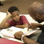 Photo of adult helping a boy in class with a paper.