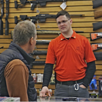 Man behind the counter of a gun shop talks to a customer.