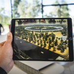 A person holding up an iPad that shows a digital world over the real world.