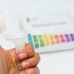 A hand holding a tube in front of a 23andMe kit