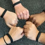 Five hands making fists in a circle. All arms have black Fitbit trackers on them.