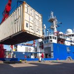 freight shipping container in foreground and research ship in background