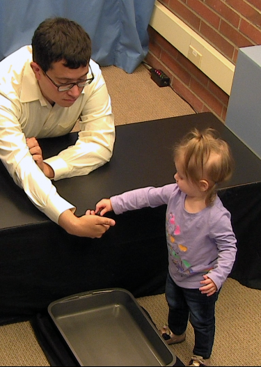 A toddler gives a blueberry to man seated at a table.