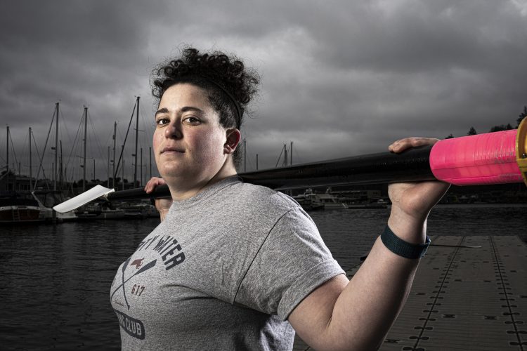 A person holds oars behind their head and looks at the camera