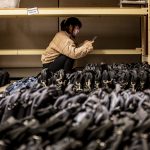 Student looks at tablet screen while crouching above rows of bagged laptops.