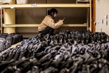 Student looks at tablet screen while crouching above rows of bagged laptops.