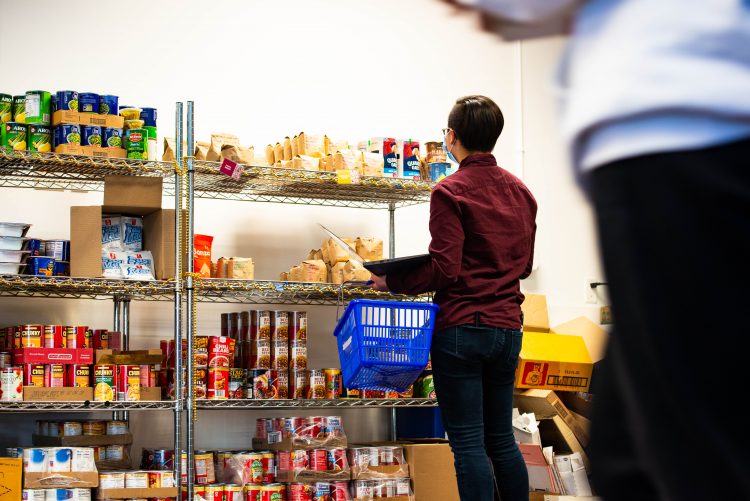 Person standing in front of shelves of food, carrying a shopping basket.