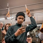A person on a train looking at their phone. Other people are on their phones behind that person.